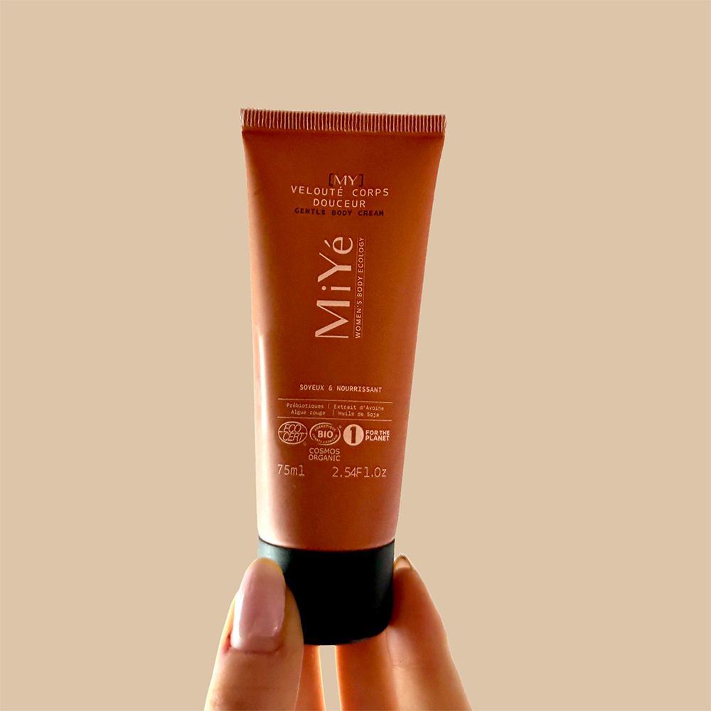 Une main tient un tube de crème pour le corps sur fond beige.