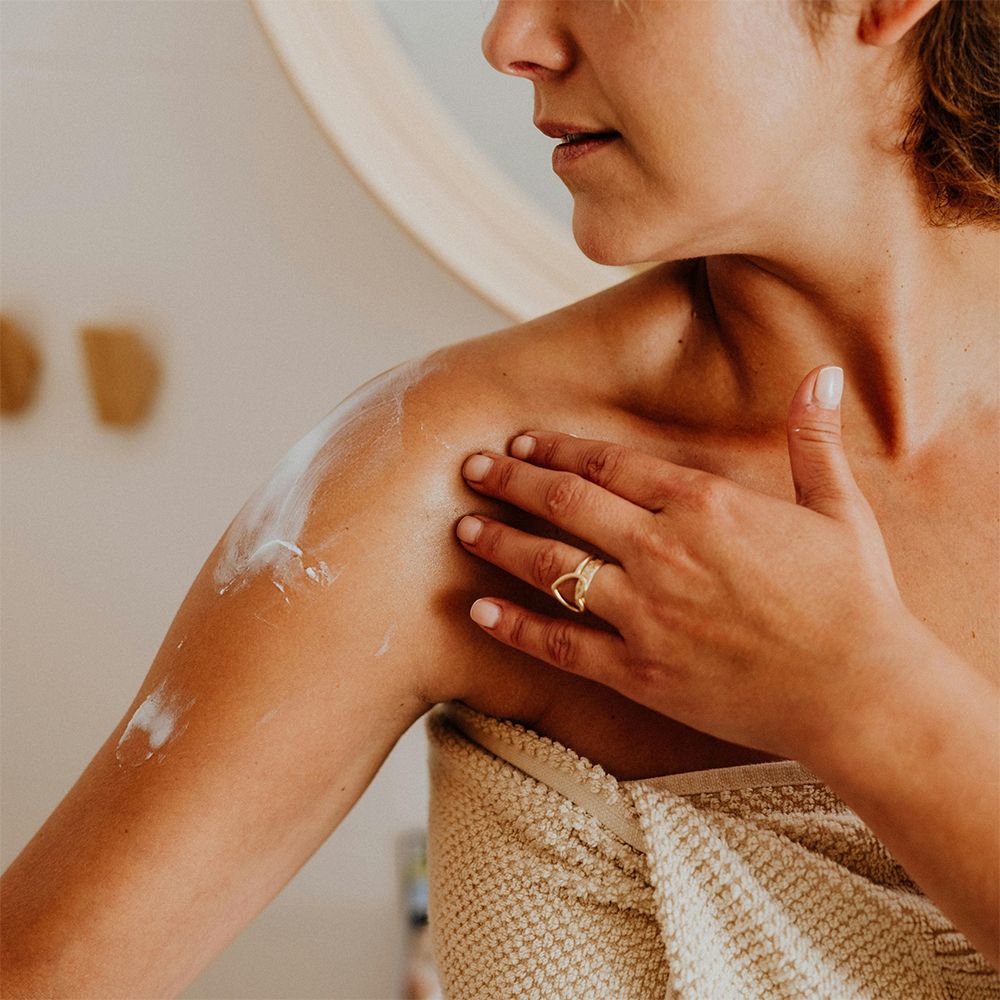 Une femme applique de la crème pour le corps sur son épaule.