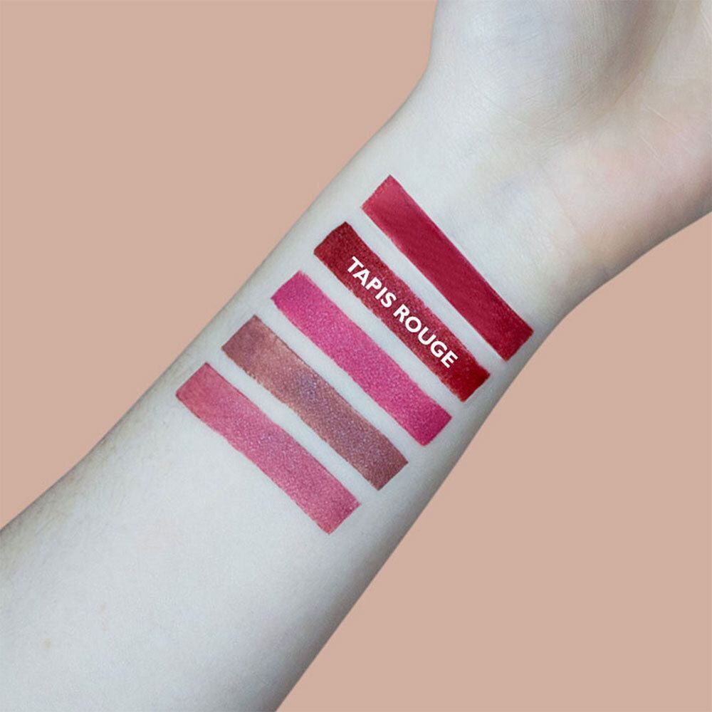Bras avec cinq échantillons de couleurs de rouge à lèvres. « TAPIS ROUGE » est écrit sur un échantillon. Les couleurs varient du rose au rouge.
