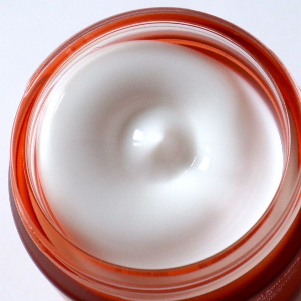 Vue de dessus d'une crème dans un pot orange. La crème est blanche et a une surface lisse.