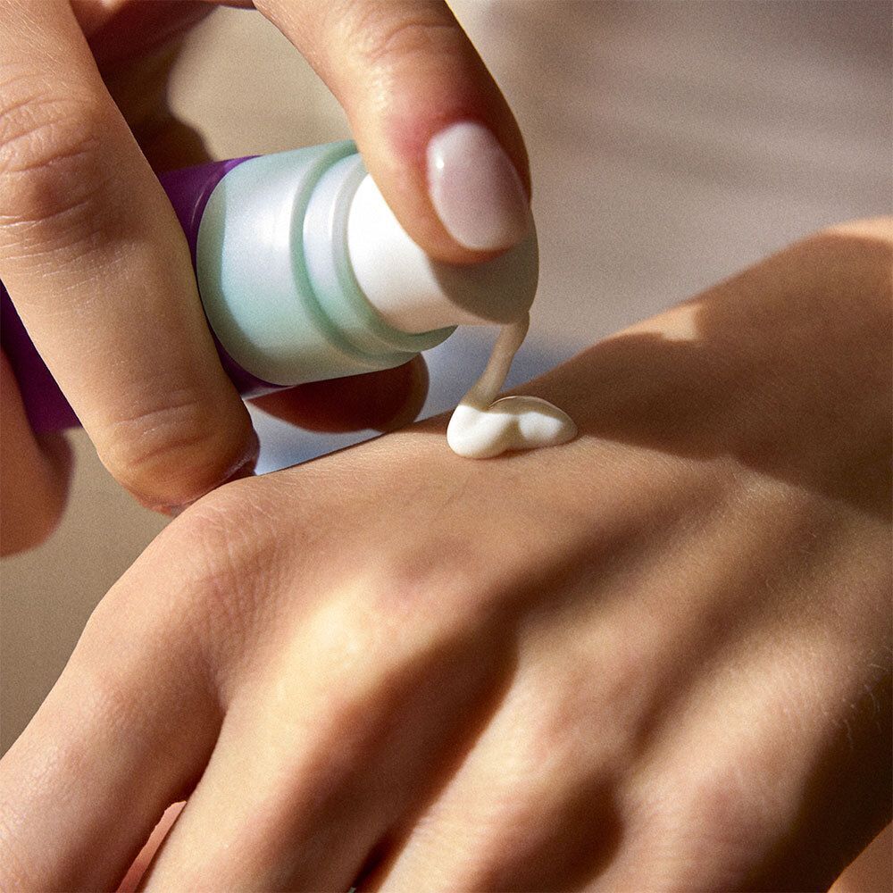 Main pressant de la crème blanche d'un tube sur la peau.