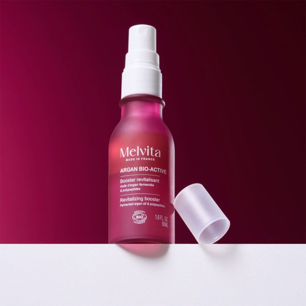 Flacon vaporisateur rose. Texte: Melvita Argan Bio-Active, Booster revitalisant. Bouchon ouvert.