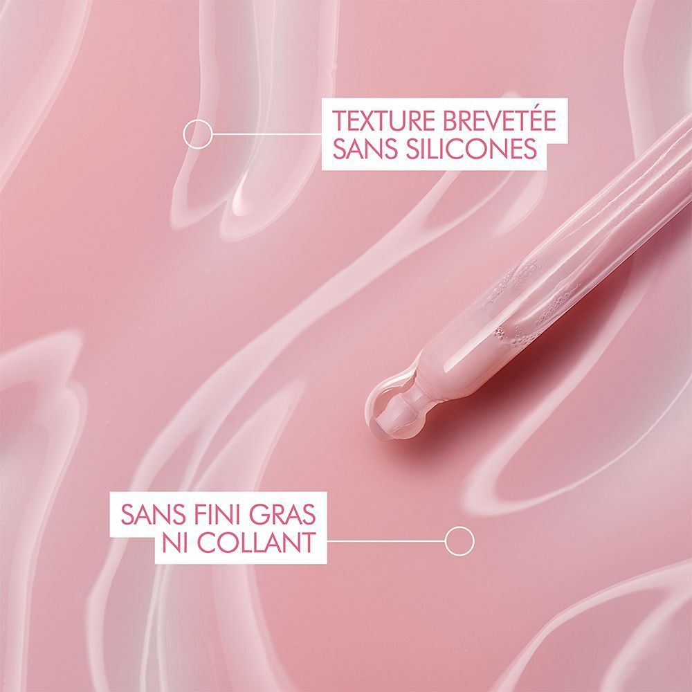 Gros plan du sérum sur fond rose. Texte: Texture sans silicones, sans fini gras ni collant.