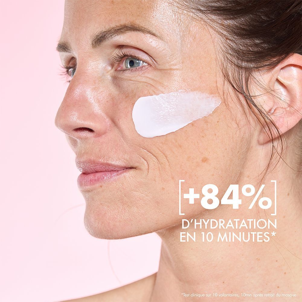 Femme avec crème sur la joue. Texte : +84% D'hydratation en 10 minutes. Fond rose.