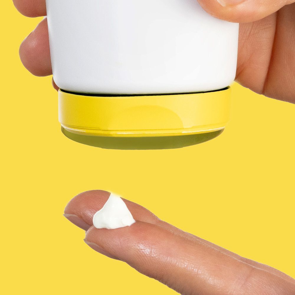 Gros plan d'une crème blanche sortant d'un tube. Base du tube jaune.