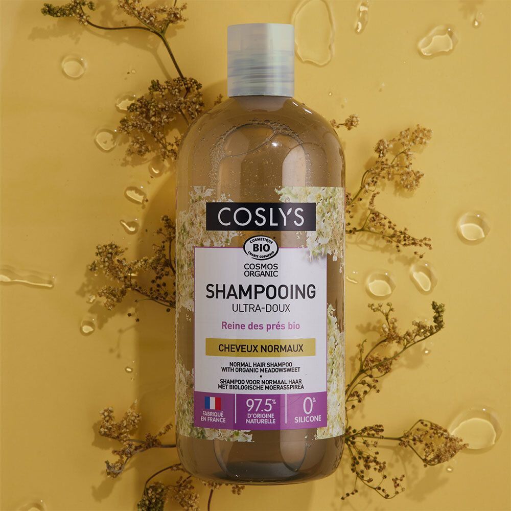 Flacon de COSLYS SHAMPOOING ULTRADOUX. Shampoo bio pour cheveux normaux. Étiquette blanche et accents verts. Sur fond jaune avec plantes.