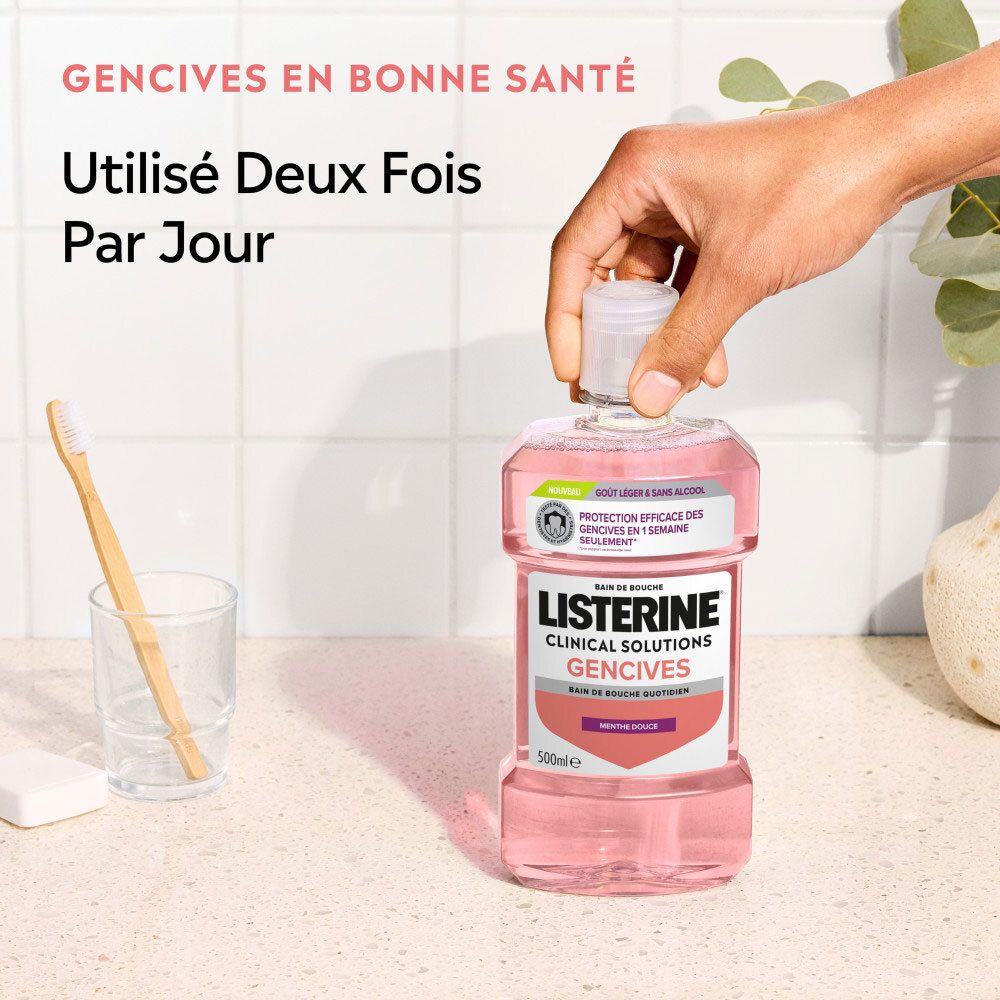 Main tenant une bouteille de Listerine Clinical Solutions Gencives Bain de Bouche près d'un verre et d'une brosse à dents.