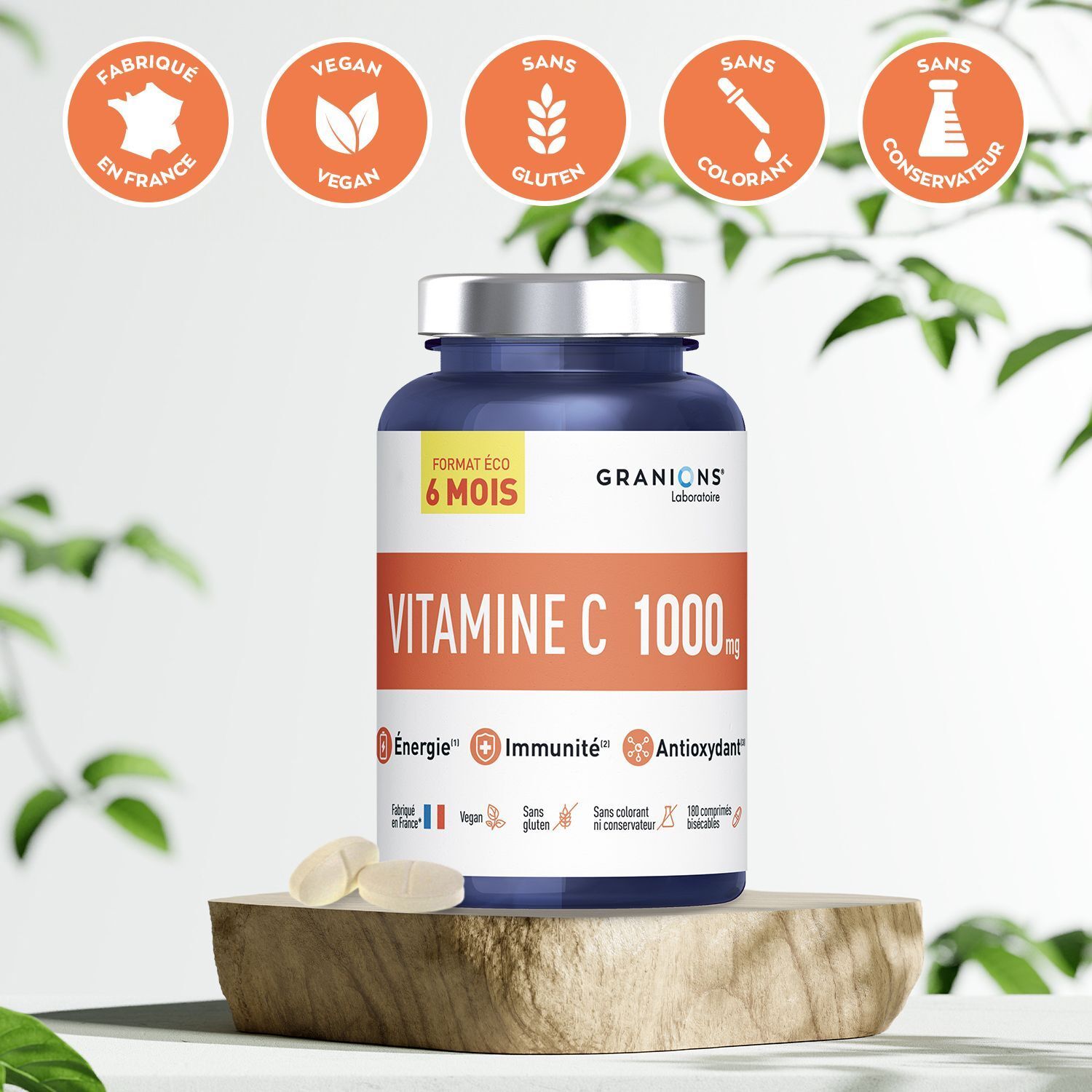 Un flacon de GRANIONS Vitamine C 1000 mg sur un socle en bois, entouré de feuilles, avec des sceaux en haut.
