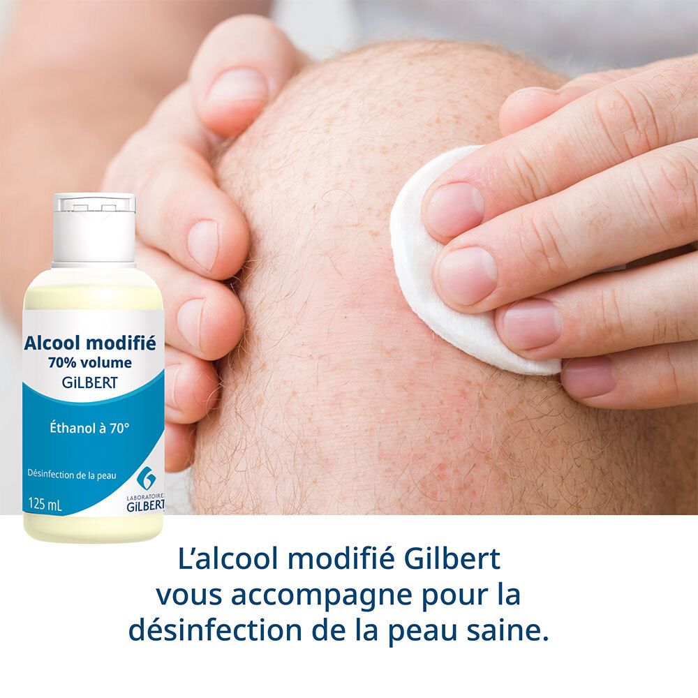 Personne désinfectant un genou avec un coton et de l'alcool. Flacon: Alcool modifié 70% volume Gilbert.