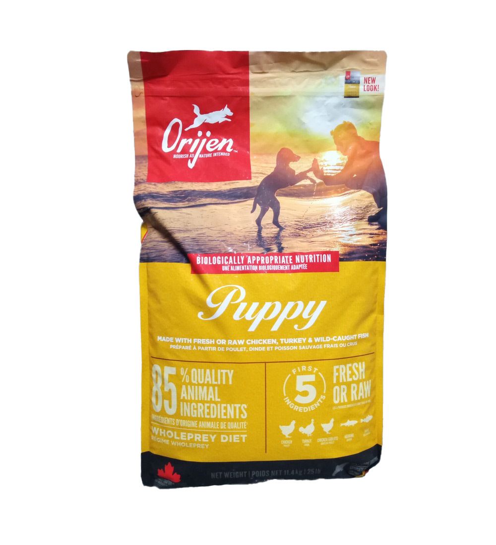 Sac jaune avec logo "Orijen" et inscription "Puppy". Contient 85% d'ingrédients d'origine animale. Image d'un chiot sur la plage.