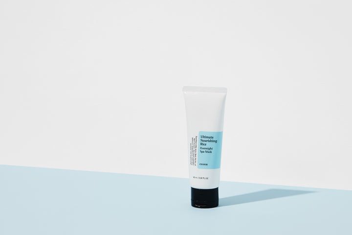Tube blanc avec bouchon noir, posé sur une table bleu clair devant un fond blanc.