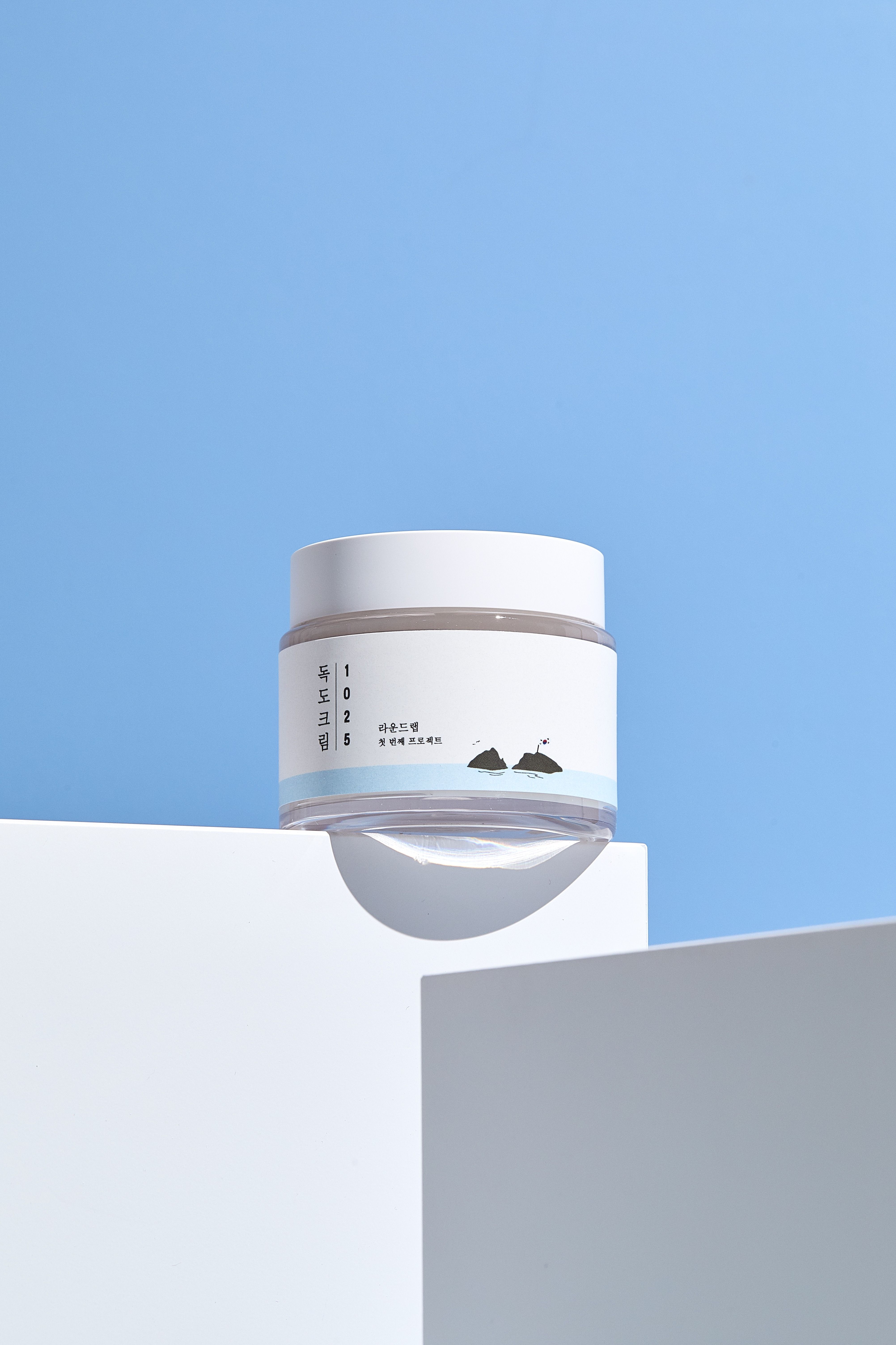 Pot de crème blanche pour la peau. Autocollant avec texte et illustration. Sur socle blanc, fond bleu.