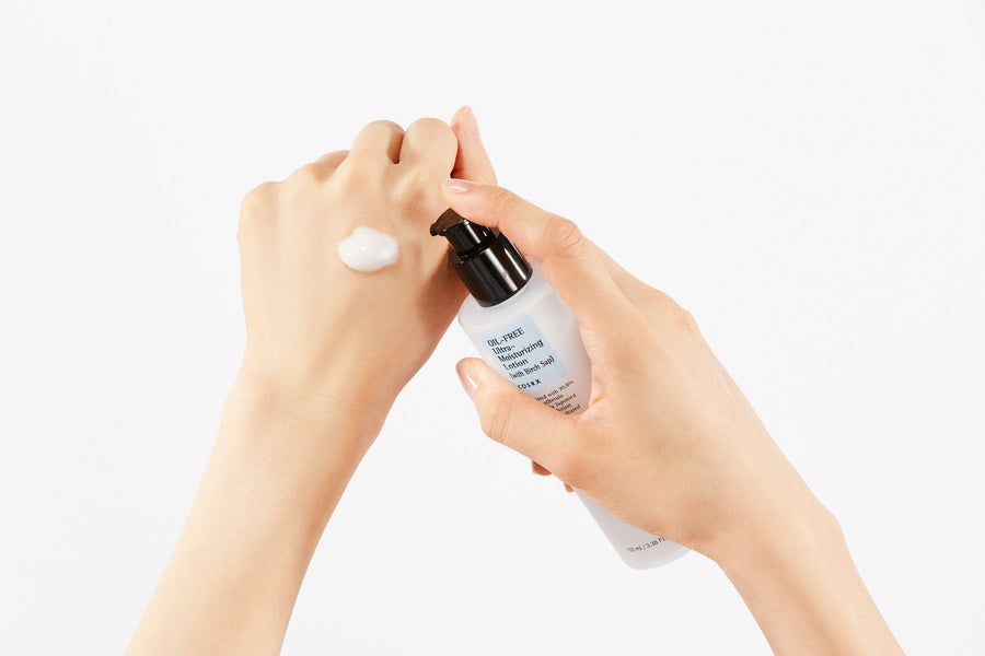 Une main dispense une lotion blanche sur l'autre main.