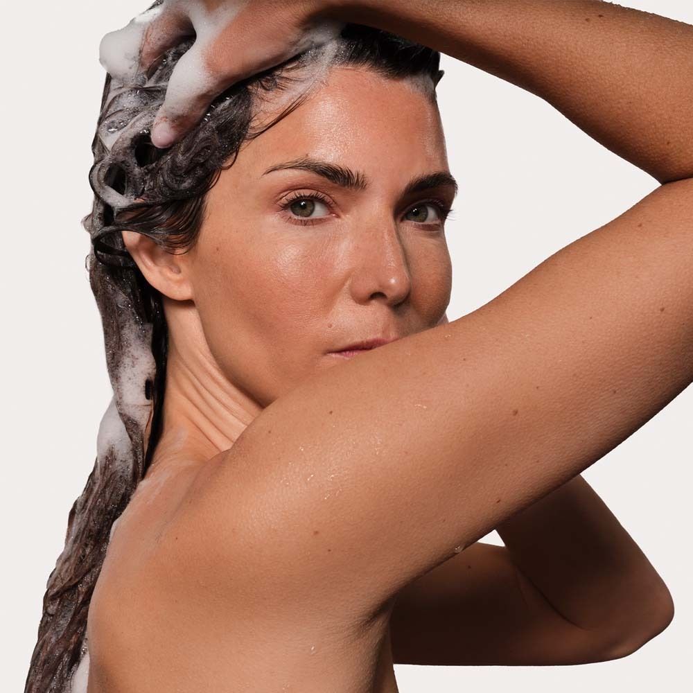 Une femme se lave les cheveux avec un shampooing moussant.