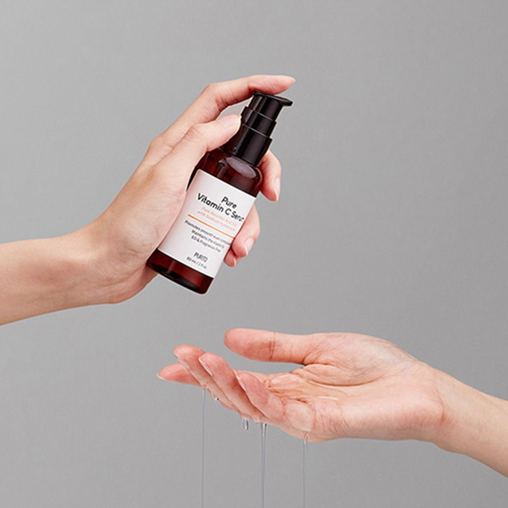 Flacon en verre brun avec pompe noire. Inscription : Pure Vitamin C Serum. Mains tenant le flacon et recevant du liquide.