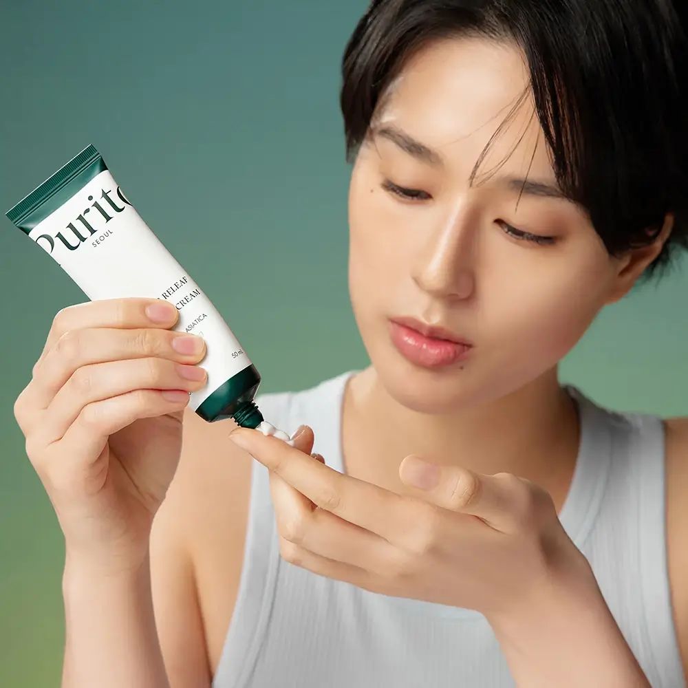 Femme pressant de la crème d'un tube sur son doigt. Inscription : PURITO, Wonder Releaf Centella Cream.