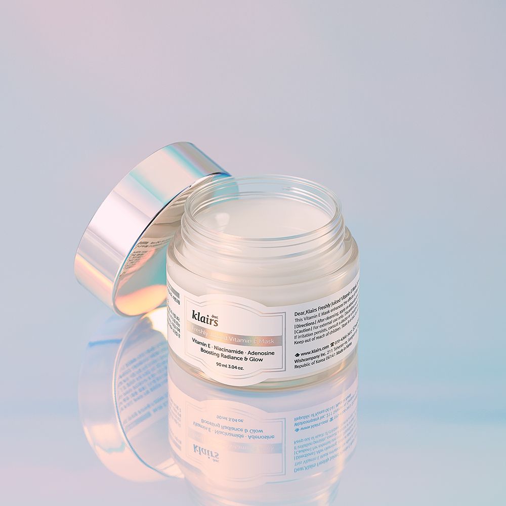 Un pot ouvert du masque à la vitamine E fraîchement pressée avec un couvercle argenté sur une surface réfléchissante.