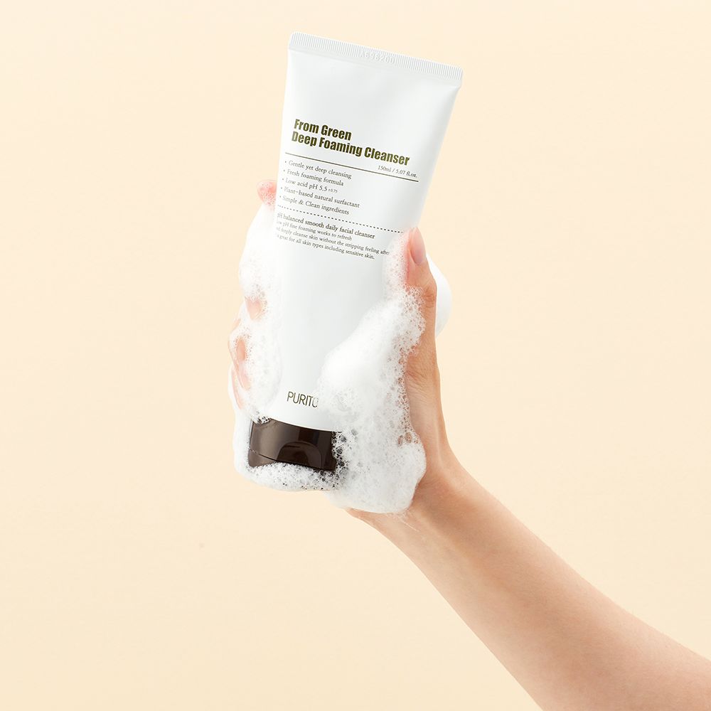 Une main tient un tube blanc de nettoyant moussant vert profond avec de la mousse.