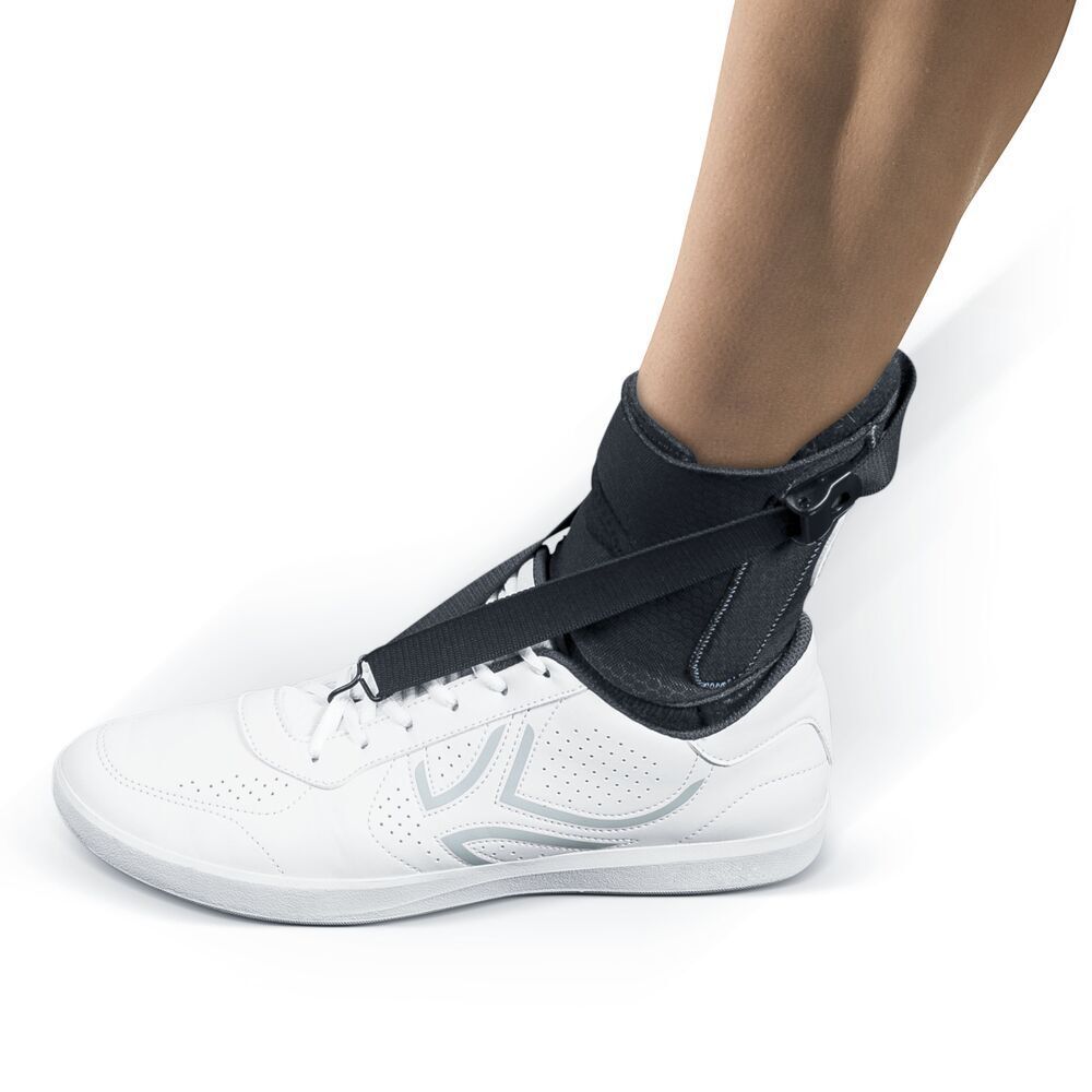 Orthèse de pied portée. Matériau textile noir, fermetures velcro et sangles. Fixée à une chaussure blanche.