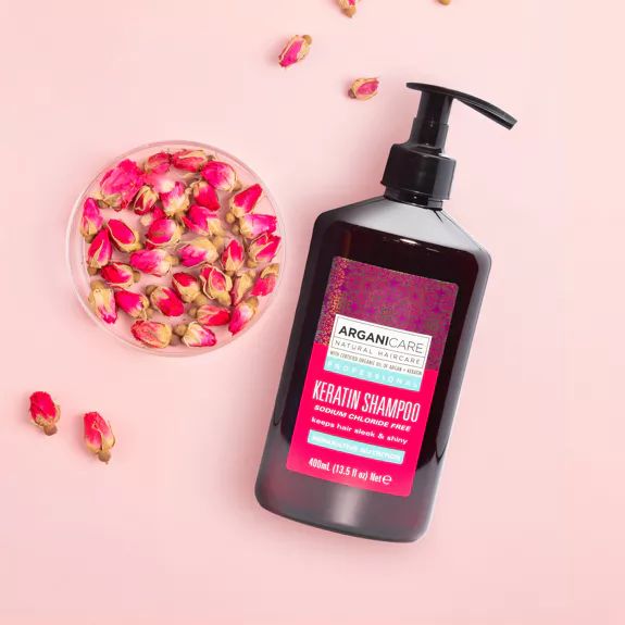 Flacon de shampooing Arganicare Keratin avec pompe. Étiquette rose avec texte. Boutons de rose à côté.