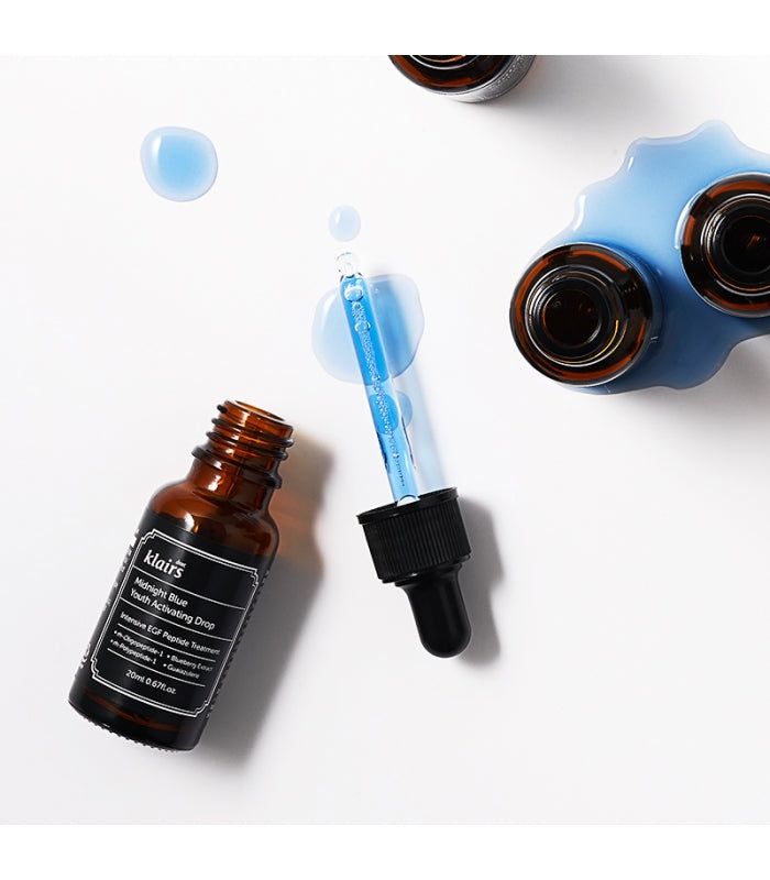 Flacon en verre brun avec étiquette noire et pipette. Liquide bleu et gouttes à côté. Nom du produit visible.