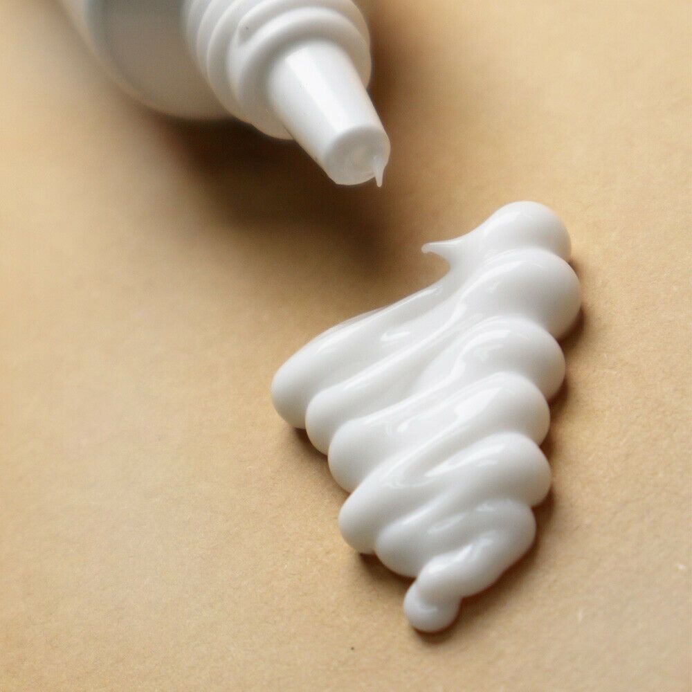 Crème contour des yeux blanche sur fond beige, appliquée à partir d'un tube.